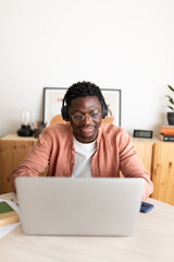 Smiling young man working from home using laptop and headphones