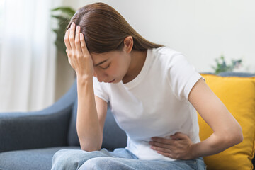 Sick asian young woman in pain, hand holding belly, stomach pain from food poisoning, girl hurt...
