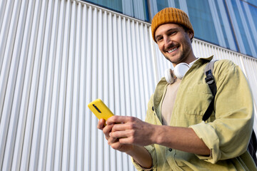 Smiling student using smartphone app in front of modern building looking at camera