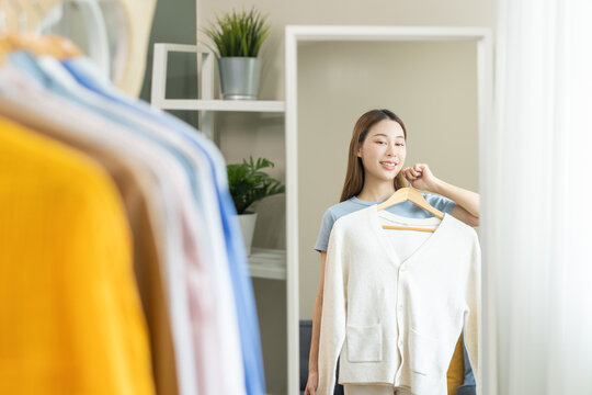 Choose clothes to wear, attractive asian young woman, girl try on appare, happy choice of shirt, female outfit on hanger in wardrobe in room closet at home. Deciding blouse what to put on which one