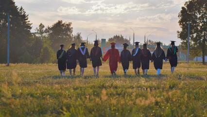 Recent graduates celebrating their academic success and friendship as they walk through a field at...