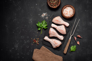 Raw chicken drumsticks with spices on black stone background, top view, flat lay