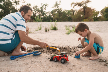 father and son building a sand castle on the beach near the water. Vacation on the coast with...