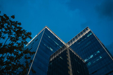 Low angle view on office building at night. Luxury real estate, urban development, and contemporary architecture against a clear blue evening sky.
