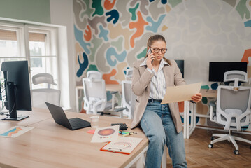 Businesswoman talking on phone and reviewing documents in modern office