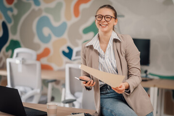 Happy businesswoman holding documents and smartphone in modern office