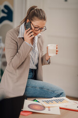 Businesswoman drinking coffee and talking on phone while reviewing charts