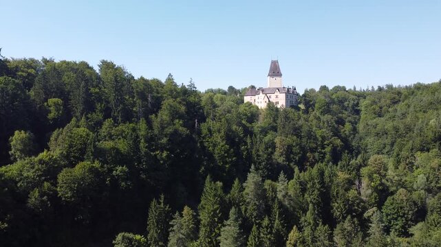 Aerial view of Schloss Ottenstein in Austria, a historic castle with a tall tower, standing above dense green forest, under clear blue skies, blending heritage with natural landscape.