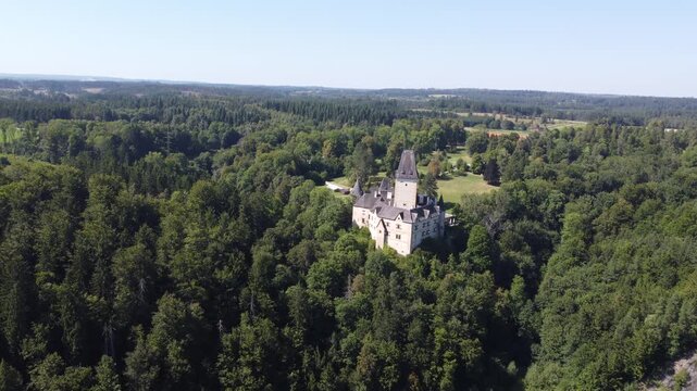 Aerial view of Schloss Ottenstein in Austria, a historic castle with a tall tower, standing above dense green forest, under clear blue skies, blending heritage with natural landscape.