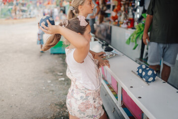 Girl throwing ball at carnival game, aiming for prize