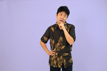 man in batik traditional shirt posing thoughtfully against purple background