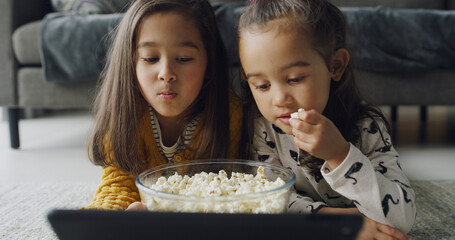 Child, siblings or watching with popcorn on tablet in home for online entertainment or subscription. People, girl or sisters streaming with technology for movie, snack or cartoon together on floor