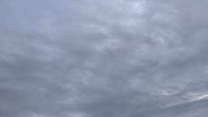 A gray, cloudy sky with a soft, uniform texture. The clouds are layered and form a dense covering,...