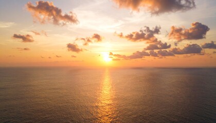 Naklejka premium Aerial view of a beautiful sunset over the calm ocean with clouds and golden light.