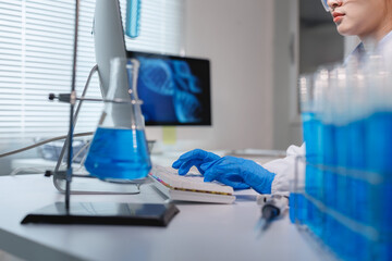 Scientist typing on keyboard in laboratory with blue chemical liquid
