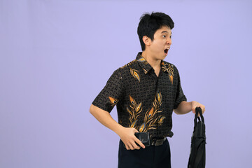 young man with batik outfit with surprised gesture holding phone in studio background