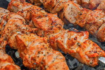 Juicy marinated skewers are being grilled over hot charcoal on metal skewers during an outdoor...