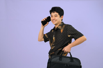 smiling individual wearing batik shirt talking on phone against plain background