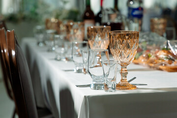 A long table covered with a white tablecloth is set with wine glasses and shot glasses. In the background, dishes and bottles are visible. The atmosphere is festive and cozy.