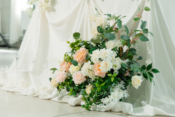 Elegant floral arrangement of white and peach roses, greenery and gypsophila on a white fabric background. Delicate and sophisticated wedding decor.