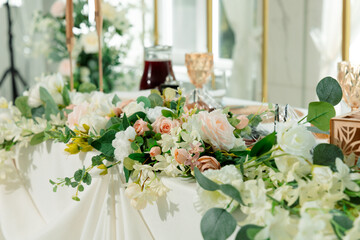 The elegant wedding table is decorated with pastel flowers: white and pink roses, greenery and...
