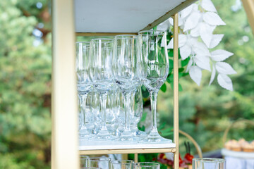 A stand with a set of elegant champagne glasses, surrounded by greenery and white flowers. The atmosphere is festive and elegant.