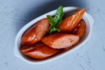 Close-up of spicy japanese sausage in a small, long white cup with a rocket leaf on top on a white background.