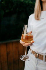 Woman is holding glass of white wine, enjoying refreshing drink on summer day against blurred wooden background. Young adult woman holding glass of white wine, relaxing during sunny summer day