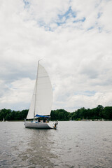 Sailboat gliding across lake, its white sail billowing against backdrop of soft, gray clouds,...
