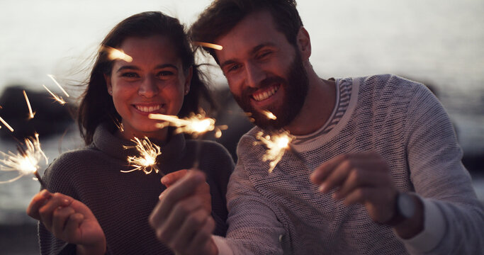 Couple, sparkler and night at beach for celebration, bonding and love on relationship anniversary. People, fireworks and excited with portrait, party or holiday by ocean for new years eve in Spain