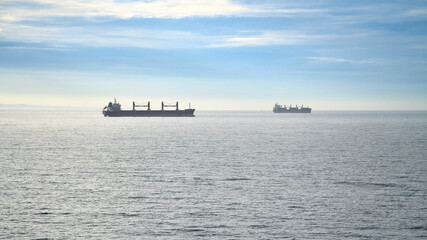 Two cargo ships glide across a calm sea under a clear sky. Minimalist seascape.