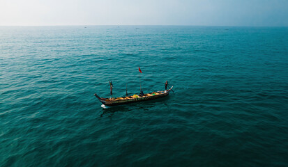 Aerial view of a small fishing boat with a red flag cutting through the vast, deep blue ocean, its wake a shimmering contrast, Ghana.