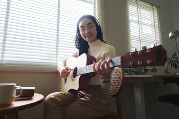 Young woman playing acoustic guitar and wearing headphones at home
