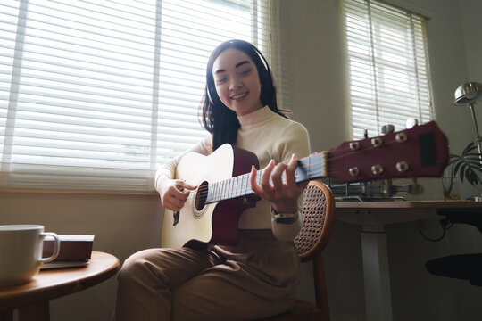 Young woman playing acoustic guitar and wearing headphones at home