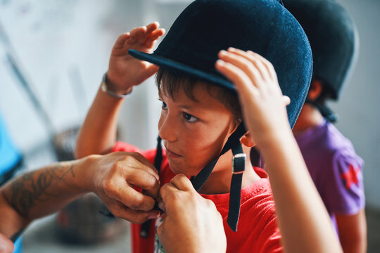 Child getting help putting on riding helmet before horseback activity