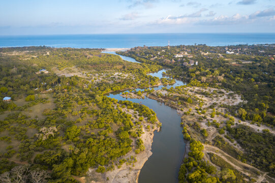 Aerial view of Kongo river snaking through lush greenery towards the turquoise ocean horizon, creating a stunning contrast of colors and textures, Tiwi, Kwale County, Kenya.
