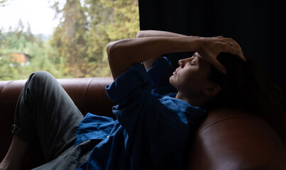 Depressed woman lying on sofa covering head with hands