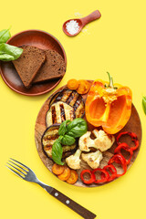 Plate with grilled vegetables and basil on yellow background