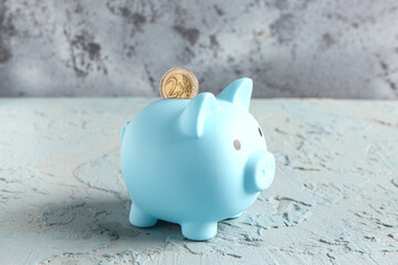 Piggy bank with coin on grunge blue table near wall