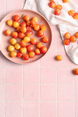 Plate with sweet yellow cherries on pink tile background