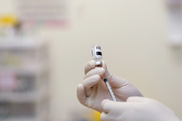 Medical professional wearing gloves holding syringe with vaccine injection for immunization and...
