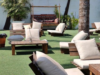 Stylish outdoor lounge with wooden chairs, white cushions, and a decorative garden sofa surrounded...