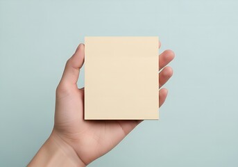 Close-up of a hand holding a blank light yellow sticky note against a soft blue background