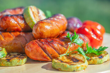 Grilled sausages with zucchini, bell pepper, and parsley on wooden board outdoors