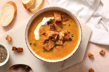 Bowl of tasty cream soup with croutons and bread on beige background