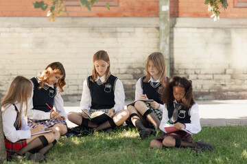 Teenage girls in plaid skirts studying outdoors sitting on grass with focus and creativity. Concept...