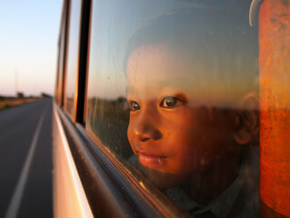 A contemplative young boy gazes out a bus window reflecting on life's journey and rural landscapes