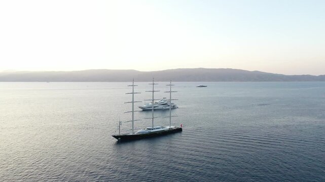 Aerial view of sailing ships cutting through the tranquil blue ocean waters near the distant landmass, a serene seascape, Idra, Nisi, Greece.