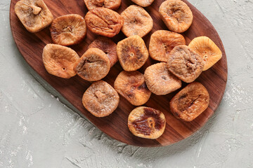 Wooden board with sweet dried figs on green background