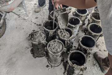 Fresh concrete being poured into cylindrical molds for strength testing at a construction site, quality control process in civil engineering.